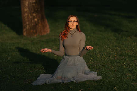 A female redhead magician holds Reiki Tibetan stones for therapy. Session of a meditation healing in the park at sunset.の写真素材