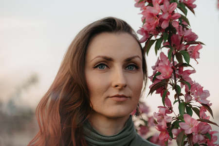 A headshot of a redhead woman is staring into the distance near flowering sakura at sunset.の写真素材