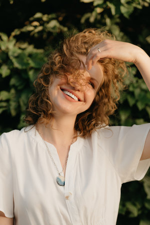 A woman with curly hair is posing in the park at the sunset.