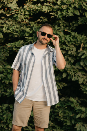 A man is posing in the garden. A guy with green leaves in the background.の写真素材