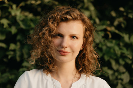 A woman with curly hair is posing in the park at the sunset.の写真素材