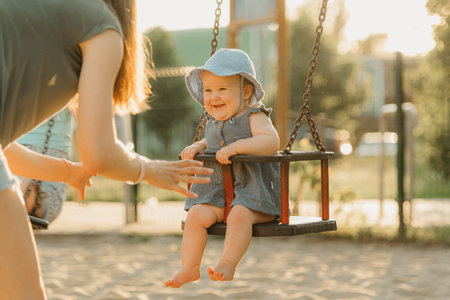 Toddler baby girl is joying on a swing on the warm summer eveningの写真素材