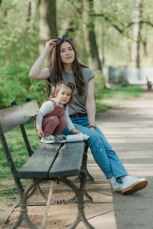 A female toddler in velvet overall is on the bench with her mother.の写真素材