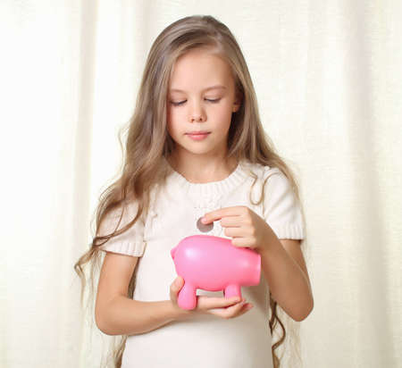 Little blond girl puts coin into piggy moneybox and dreaming about future purchaseの写真素材