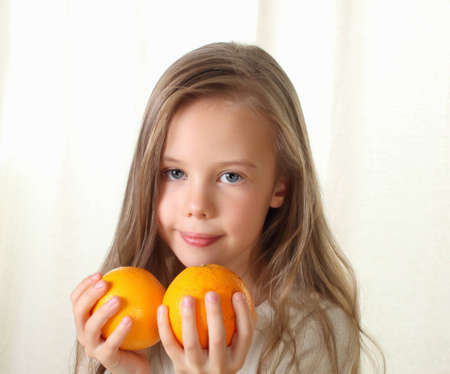 Little blond girl with oranges smiling and looking to cameraの写真素材