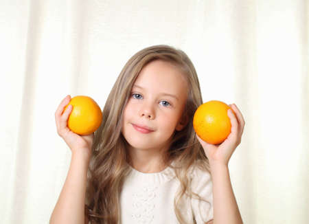 Little blond girl with oranges smiling and looking to cameraの写真素材