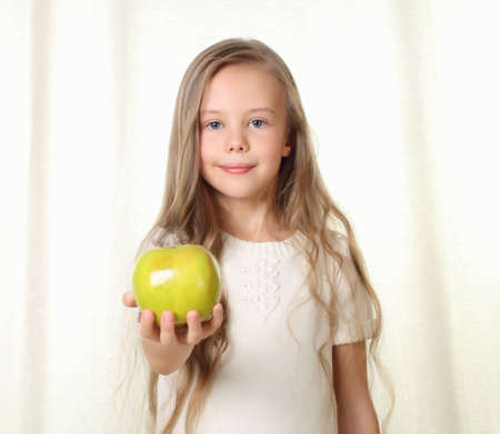 Little blond girl with apple shows in to cameraの写真素材