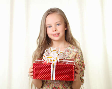Little blond girl holding a red glamorous gift ang looking to cameraの写真素材