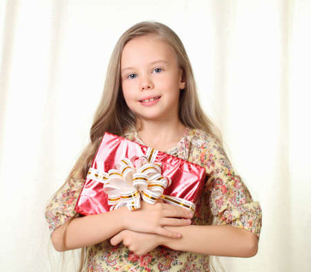 Little blond girl holding a red glamorous gift and smilingの写真素材