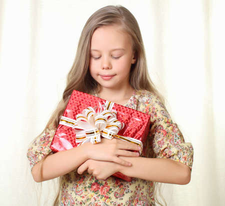 Little blond girl holding a red glamorous gift with pleasureの写真素材