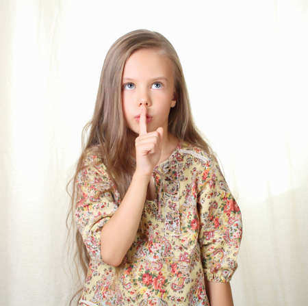Little blond girl keepeing silence holding forefinger near lipsの写真素材