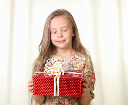 Little blond girl holding a red glamorous gift and looking on itの写真素材