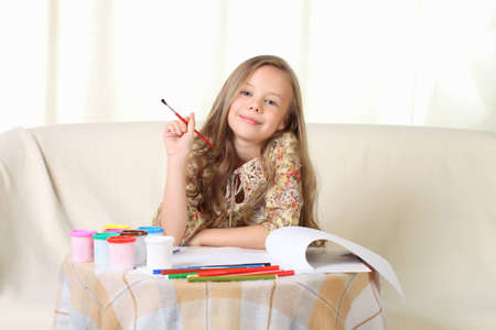Little blond girl drawing at home on sofa and looking aboveの写真素材