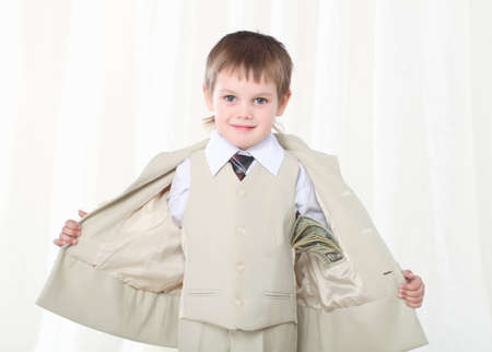 Little smart boy in suit showing dollars inside internal pocketの写真素材