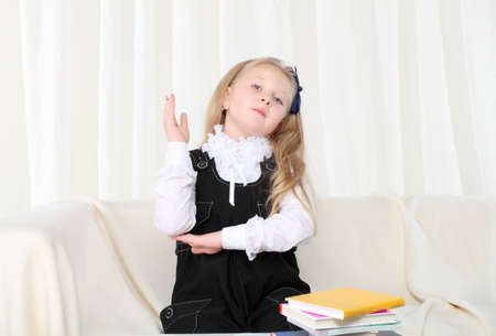 Little girl rised hand near books sitting on sofaの写真素材