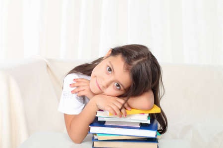 Little girl laying on books sitting on sofa in sad moodの写真素材