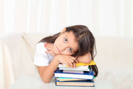 Little girl laying on books sitting on sofa in sad moodの写真素材