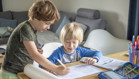 Two boys learning at home in living room, older one helps the younger oneの写真素材