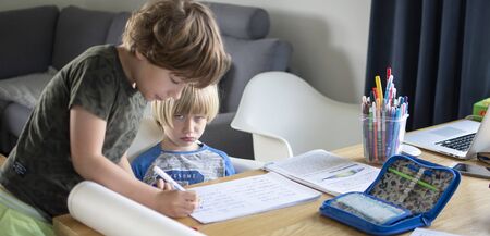 Two boys learning at home in living room, older one helps the younger oneの写真素材
