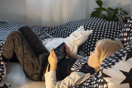 boy playing / watching something on tablet in bed in the eveningの写真素材
