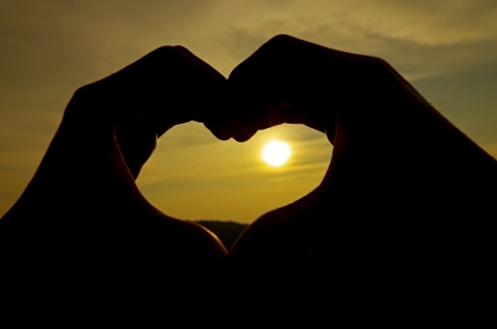 Heart silhouette by hand on sunrise backgroundの写真素材