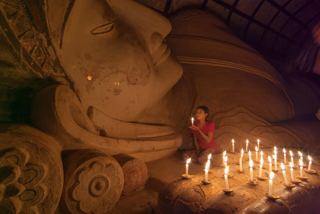 BAGAN, MYANMAR - JAN 5, 2011: Unidentified Burmese girl praying with candle light in a Buddihist temple on January 5, 2011 in Bagan, Myanmar. 89% of the Burmese population is Buddhist.のeditorial素材