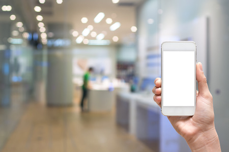 Female hand holding mobile smart phone on store blur with bokeh background, business concept Female hand holding mobile smart phone on store blur with bokeh background, business concept