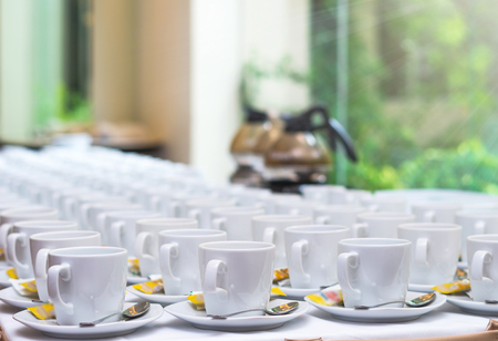 Many rows of white coffee cup with saucer and teaspoon on table and coffee maker の写真素材