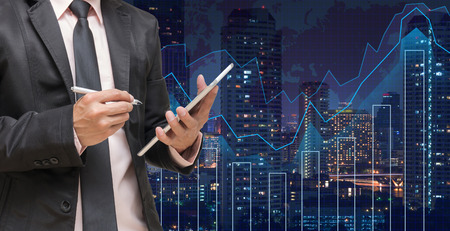 Businessman using the tablet on Trading graph on the cityscape at night and world map background,Business financial concept Businessman using the tablet on Trading graph on the cityscape at night and world map background,Business financial concept