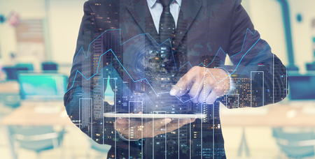 Double exposure of businessman using the tablet with cityscape and financial graph which have earth and world map on computer blurred background