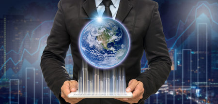 Businessman holding the tablet with earth and building on Trading graph on the cityscape at night and world map background,Elements of this image furnished by NASAの写真素材