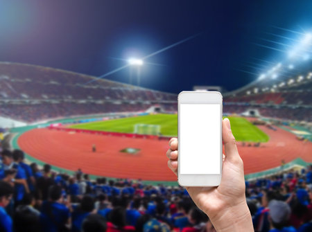 Hands holding smart mobile taking photo on the Abstract blurred photo of soccer stadium, sport background conceptの写真素材