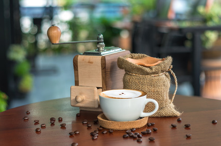 Cappuccino coffee cup on wood table with traditional coffee beans and grinderの写真素材
