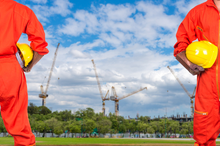 Asian engineers holding a yellow hardhat on Under construction four cranes with cloud on blue sky, constructure industrial conceptの写真素材