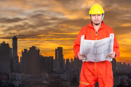 Asian engineers worker looking at the blueprint on Building of cityscape at sunrise background,...