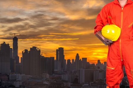 Asian engineers worker holding a yellow hardhat on Building of cityscape at sunrise background, industrial conceptの写真素材