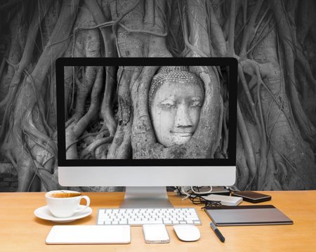Conceptual image of a workspace with computer desktop on Head of sand stone buddha in a tree at Wat...