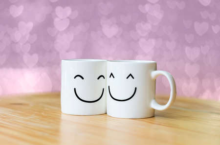 Two happy cups on wood table with Valentine's day hearts bokeh backgroundの写真素材