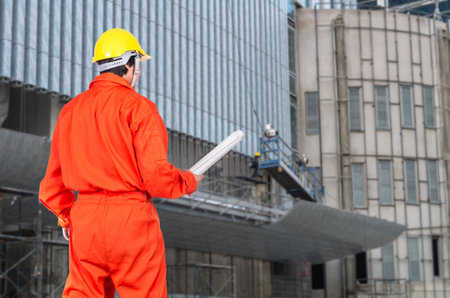 Portrait of Asian engineers holding at the blueprint on photo blurred of construction site workers,...