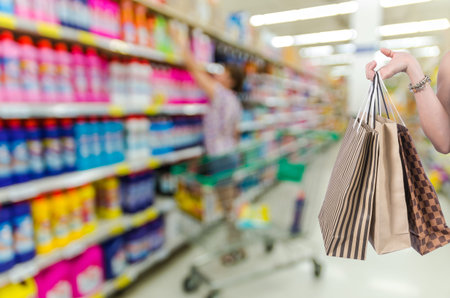 Holding shopping bags by hand on Supermarket with Abstract blurred photo of store with trolley in department store bokeh backgroundの写真素材