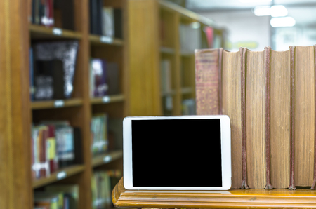 Tablet computer with old books on the wood table in library, Education conceptの写真素材