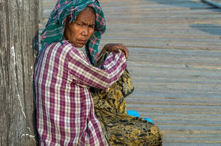 MANDALAY, MYANMAR - MARCH 13 : Unidentified Old woman sitting at the ubein bridge on March 13, 2016 in Mandalay, Myanmar. The U-Bein bridge is the longest teak bridge in the world, 1.2km length.のeditorial素材