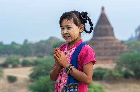 Burmese girl with traditional thanaka on her face praying on pagoda blurred background at bagan in Mandalay, Myanmarの写真素材
