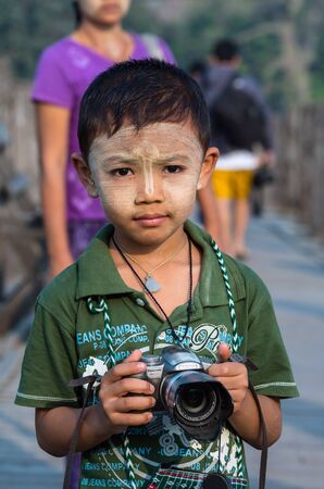 MANDALAY, MYANMAR - MARCH 13 : Unidentified Burmese boy holding the camera at the ubein bridge on March 13, 2016 in Mandalay, Myanmar. The U-Bein bridge is the longest teak bridge in the world, 1.2km length.のeditorial素材