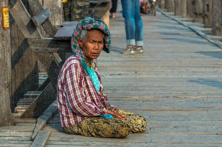 MANDALAY, MYANMAR - MARCH 13 : Unidentified Old woman sitting at the ubein bridge on March 13, 2016 in Mandalay, Myanmar. The U-Bein bridge is the longest teak bridge in the world, 1.2km length.のeditorial素材