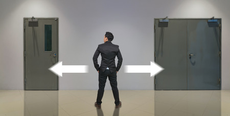 Businessman standing in doubt,thinking the two different choices indicated by arrows pointing in opposite direction, business decision conceptの写真素材