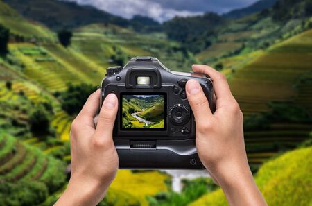 Hands holding the camera which taking photo of Rice fields on terraced of Mu Cang Chai District at sunrise time, YenBai province, Northwest Vietnam, worm toneの写真素材