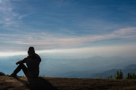 silhouette of a man who sitting and looking over the mountains landscape backgroundの写真素材