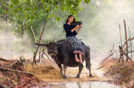 Asian rural woman listening the song via vintage music player on the buffalo at the countryside, soft focus and color tone style process, Countryside Lifestyle conceptの写真素材