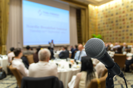 Microphone over the Abstract blurred photo of conference hall or seminar room with attendee backgroundの写真素材
